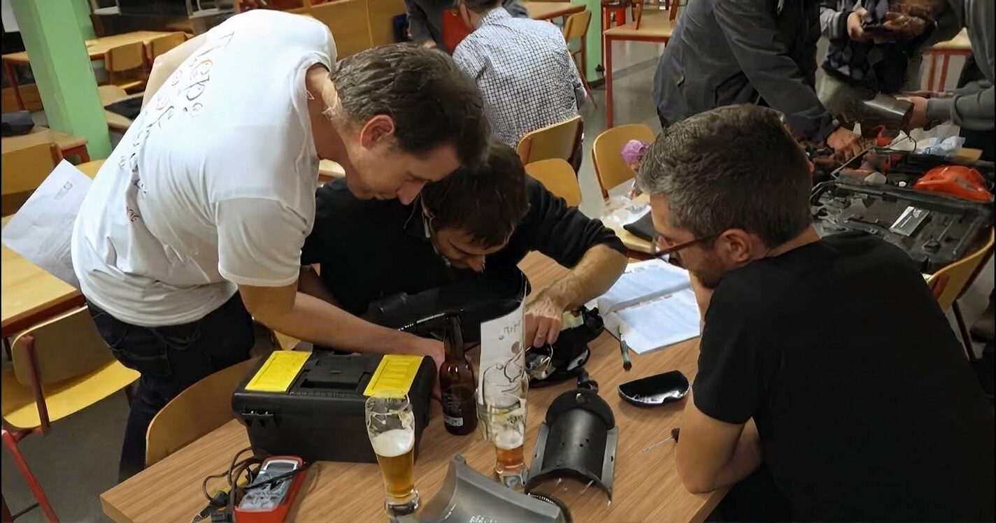 Plusieurs personnes rassemblées autour d'une table démontent et réparent
                ensemble un appareil, entourées de boîtes à outils et de verres, dans une ambiance conviviale